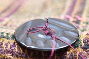 fixation d'un bouton sur un tissu de laine à l'aide d'une aiguille photo