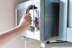 la main ferme le four à micro-ondes pour la cuisson des aliments photo