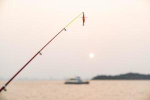 petit poisson artificiel sur une canne à pêche avec fond de mer, pêche au coucher du soleil. photo