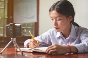 une étudiante avec un costume d'étudiant étudie en ligne à partir d'un téléphone portable à la maison avec l'enseignant, notez que l'enseignant explique les connaissances sur son livre, l'éducation et le concept d'apprentissage en ligne copiez l'espace pour le texte photo