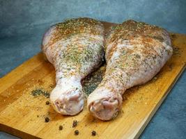 les pilons de dinde aux épices se trouvent sur une planche à découper de cuisine. viande de volaille. jambe de dinde. la viande juteuse attend d'être cuite. en attendant le four. photo