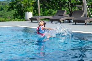 petite fille joue dans la piscine extérieure du complexe tropical pendant les vacances d'été en famille. les enfants apprennent à nager. activités estivales saines pour les enfants. photo