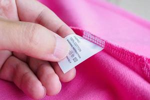 Femme lisant sur l'entretien de la lessive instructions de lavage étiquette de vêtements sur chemise en coton rose photo