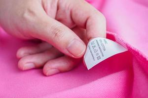 Femme lisant sur l'entretien de la lessive instructions de lavage étiquette de vêtements sur chemise en coton rose photo