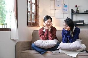 heureuses amies asiatiques à la maison assises sur un canapé. deux jeunes femmes discutant sur un canapé, bavardant et partageant des secrets discutant de la vie et des relations. concept de confiance d'amitié photo