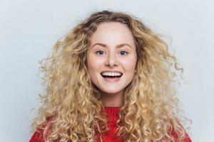 portrait horizontal d'une heureuse adorable femme heureuse avec un look attrayant, se sent excitée en entendant une histoire amusante et intéressante, isolée sur fond blanc. femme ravie souriante avec une coiffure bouclée photo