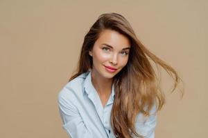 portrait d'une jeune femme séduisante a des cheveux blonds flottant dans le vent, une beauté naturelle, porte du maquillage, vêtue d'une chemise élégante, isolée sur fond marron, a une peau saine. gens, style, féminité photo