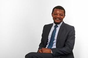 homme noir afro-américain souriant en costume d'affaires assis sur une chaise isolée sur fond blanc photo