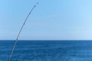 canne à pêche sur fond bleu océan ou mer, espace de copie. en attente du plus gros butin. sport relaxant méditatif. photo