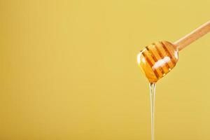 le miel doré s'écoule d'une louche à miel en bois sur fond jaune photo