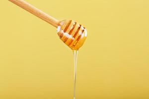 le miel coule dans un mince filet d'une louche de miel sur fond jaune. photo