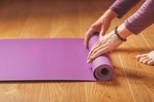 un homme pose un tapis de yoga lilas sur le parquet d'une maison