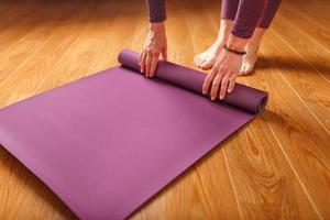 une femme pose un tapis de yoga lilas sur le parquet. photo