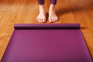les pieds de la fille se tiennent devant un tapis de yoga déplié sur le parquet. photo