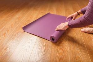 les mains d'une femme disposent d'un tapis de yoga ou de fitness lilas avant une séance d'entraînement à la maison sur un sol en bois. photo