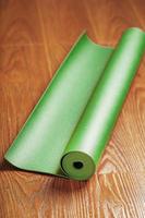un tapis de yoga vert est disposé en rouleau sur le parquet.