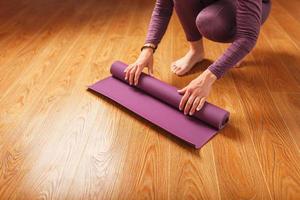 les mains d'une femme disposent d'un tapis de yoga ou de fitness lilas avant une séance d'entraînement à la maison sur un sol en bois. photo