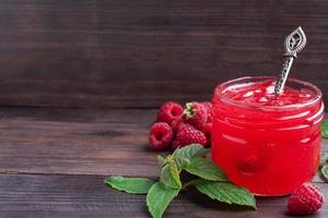 confiture de framboises maison dans un bocal en verre et framboises fraîches à la menthe sur fond rustique en bois. copie espace photo