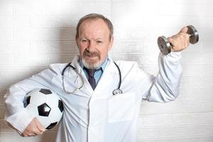 médecin souriant tenant un ballon de football dans une main et un haltère dans l'autre. animation sportive. photo