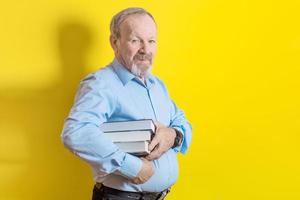 homme âgé souriant tenant une pile de livres dans ses mains sur fond jaune photo