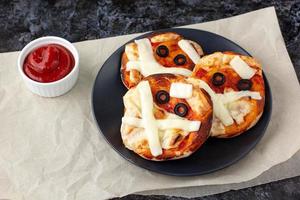 mini pizza comme momie pour les enfants avec du fromage, des olives et du ketchup. drôle de nourriture folle d'halloween pour les enfants. photo