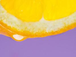 photo macro d'une goutte de jus d'orange sur une tranche d'orange sur fond violet