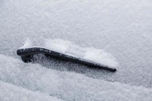 Pare-brise arrière de voiture et lame d'essuie-glace gelée et recouverte de neige à la lumière du jour nuageux d'hiver photo