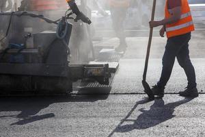 hommes travaillant avec une machine à asphalter pendant les travaux de réparation de la rue à la lumière du jour avec de la fumée et de la vapeur dans l'air photo