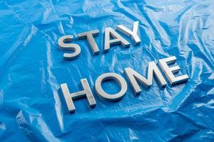 les mots rester à la maison posés avec des lettres en métal argenté sur fond de plastique bleu froissé dans une perspective diagonale inclinée photo