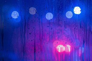 un fond abstrait de feux de rue de nuit rouge, violet et bleu bokeh à travers le verre humide avec mise au point sélective photo