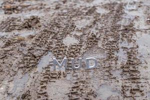 le mot boue composé de lettres en métal argenté sur une surface de terre humide photo