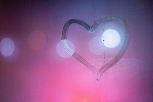 symbole de coeur dessiné à la main sur une vitre de nuit humide dans des couleurs roses photo