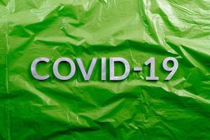 le mot covid-19 posé avec des lettres en aluminium sur fond de film plastique vert froissé dans une composition à plat, directement au-dessus de la vue photo