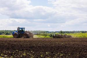 tracteur bleu avec roues doubles tirant une herse à disques avec panier à rouleaux lors d'une chaude journée ensoleillée photo