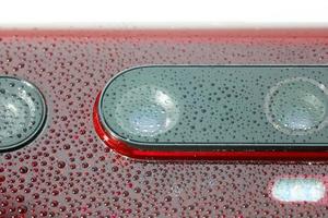 objectif de l'appareil photo du téléphone rouge recouvert de petites gouttes d'eau - gros plan avec mise au point sélective et flou