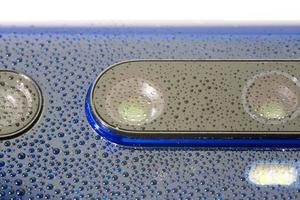 objectif de l'appareil photo du téléphone bleu recouvert de petites gouttes d'eau - gros plan avec mise au point sélective et flou