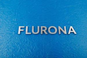 le mot flurona posé avec des lettres en métal argenté sur fond de film plastique bleu froissé photo