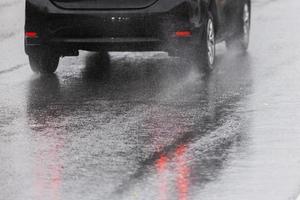 les éclaboussures d'eau de pluie s'écoulent des roues d'une voiture noire se déplaçant rapidement dans la ville de la lumière du jour photo