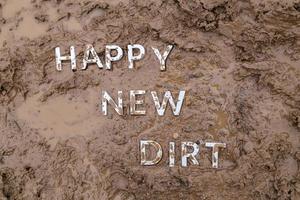 les mots happy new dirt posés avec des lettres en métal argenté sur la surface de la boue humide photo