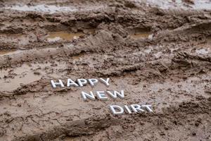 les mots happy new dirt posés avec des lettres en métal argenté sur la surface de la boue humide photo