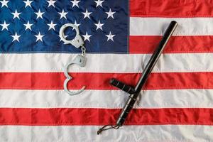 menottes en métal argenté et matraque de police sur le drapeau américain sur une surface plane photo