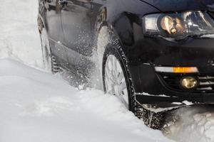 un véhicule noir se déplaçant dans la neige profonde dérape, la roue de la voiture tourne et crache des morceaux de neige, il tente de gagner en traction sur la route glissante. photo