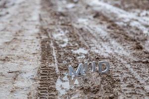 le mot boue composé de lettres en métal argenté sur une surface de terre humide photo