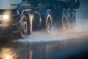 les éclaboussures d'eau de pluie s'écoulent des roues d'un camion lourd se déplaçant rapidement dans la ville de la lumière du jour avec une mise au point sélective. photo