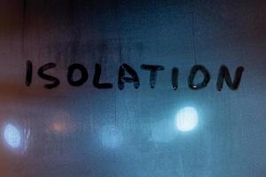 le mot isolement manuscrit avec le doigt sur la vitre de la nuit brumeuse avec des lampadaires flous sur l'arrière-plan photo