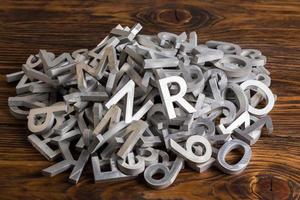 tas de caractères de l'alphabet en métal argenté coupés par une machine à jet d'eau sur fond de bois photo