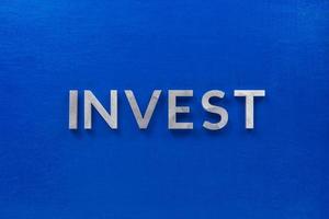 le mot investir posé avec des caractères en métal argenté sur une planche en bois peinte en bleu dans la composition centrale à plat photo