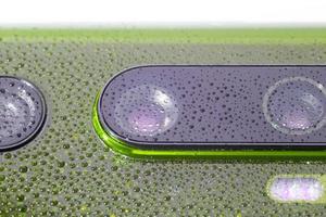 objectif de l'appareil photo du téléphone vert recouvert de petites gouttes d'eau - gros plan avec mise au point sélective et flou