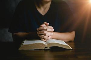 main de personne de prière sur fond noir. une femme catholique chrétienne prie Dieu dans le noir à l'église. fille croit et foi en jésus christ. la religion du christ et le christianisme adorent ou prient le concept. photo