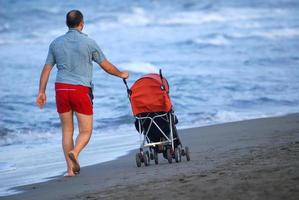 père avec poussette tôt le matin marchant sur la plage photo